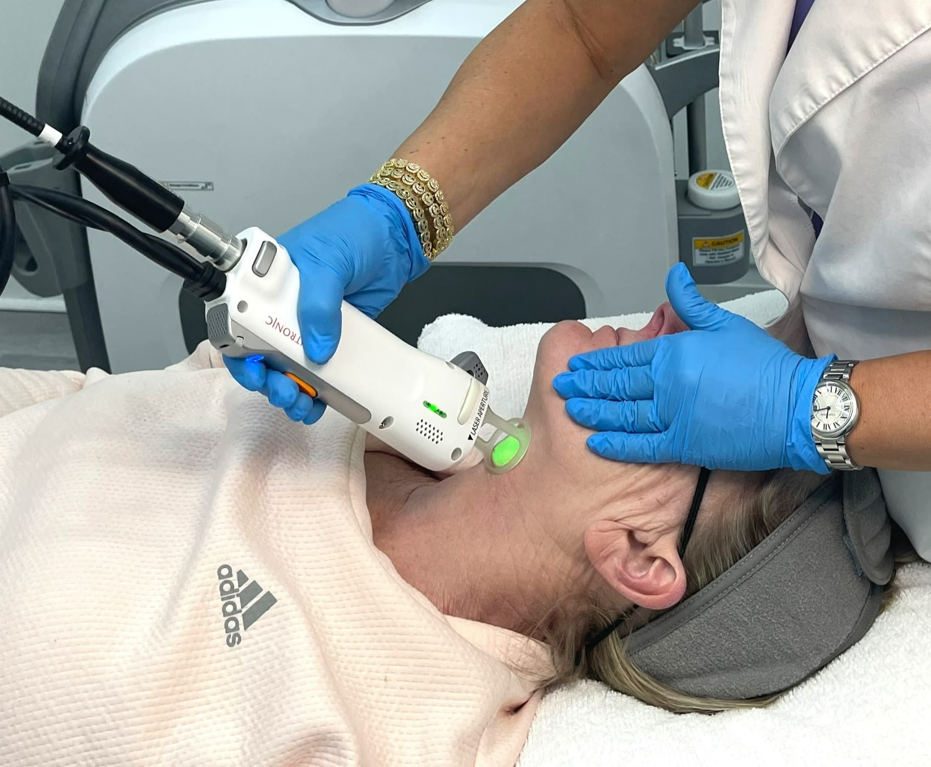 Skin rejuvenation laser treatment being done on woman lying on examination bed by laser technician